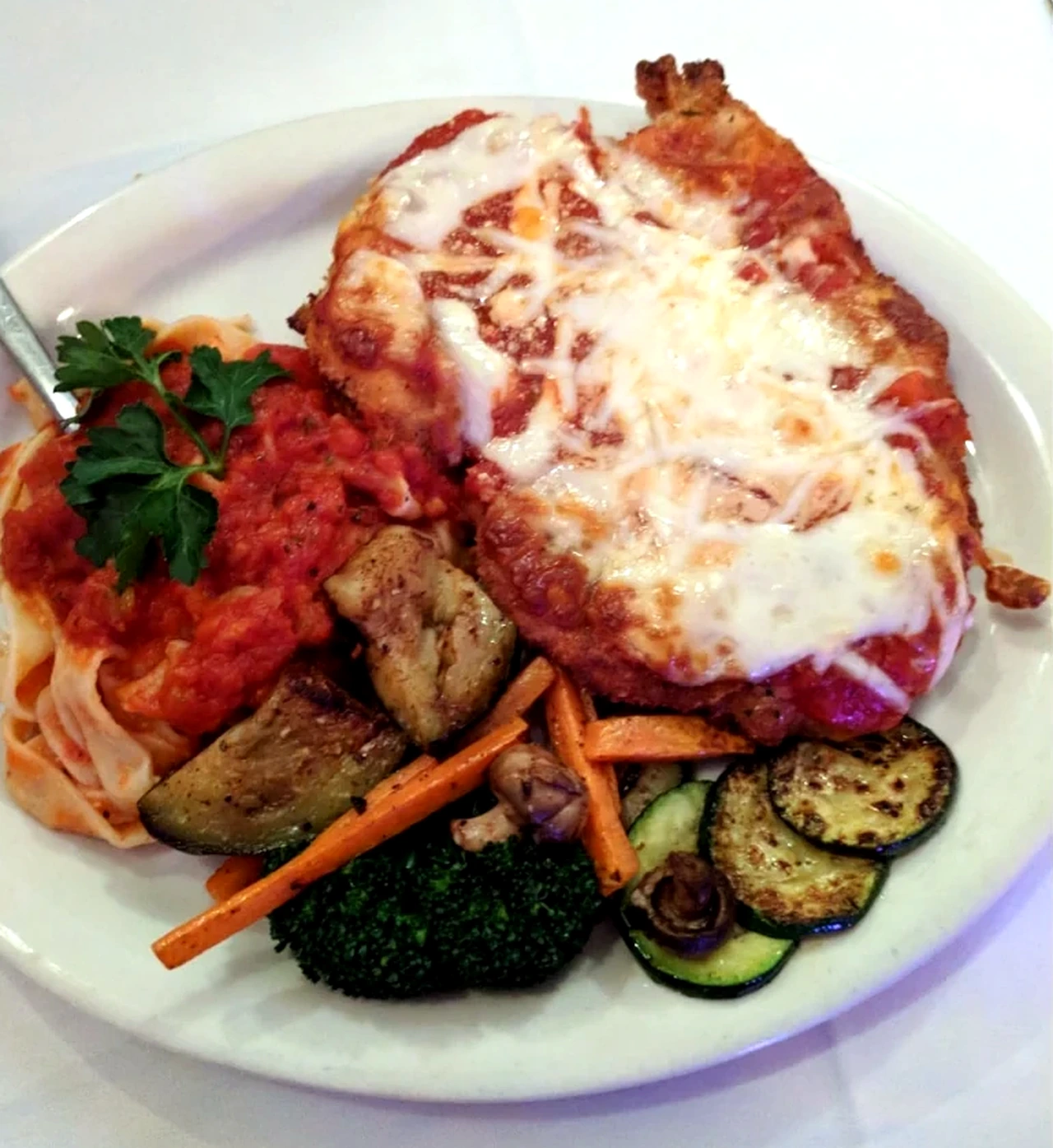 Chicken parmigiana served with pasta and vegetables